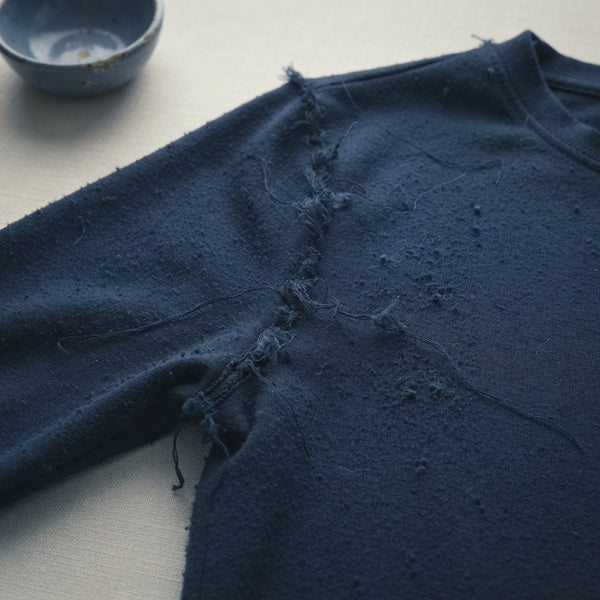 Close-up of a worn-out garment with frayed seams and loose threads on a cream surface.