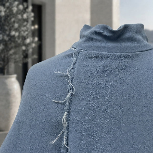 Close-up of a damaged garment showing a frayed seam and pilling fabric to illustrate poor clothing durability.